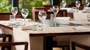 Een restaurant met gedekte tafels, grote ramen en uitzicht op groen.