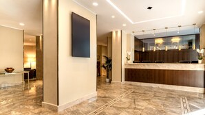 Een moderne lobby met een receptiebalie, een grote wandtelevisie en een potplant.