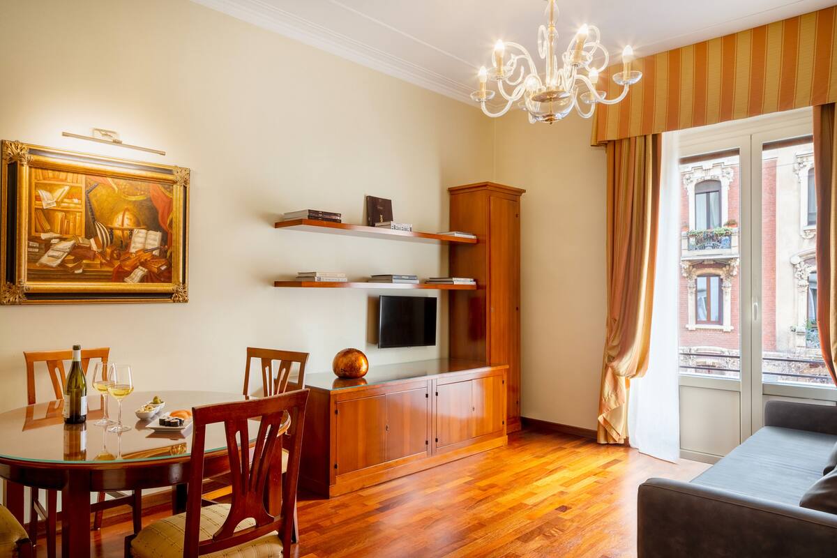 Uma sala de jantar com mesa de madeira, cadeiras, um lustre e um quadro na parede.