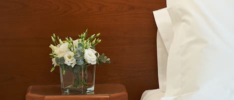 A hotel room with a bedside lamp, a small table with a vase of flowers, and a bed with white linens.