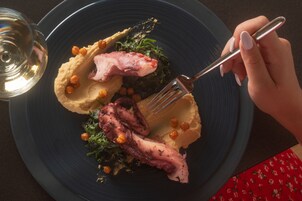 A plate with octopus, chickpeas, and greens, accompanied by a fork and a glass of white wine.