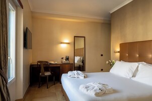 Habitación de hotel con cama, escritorio, silla, cafetera y televisor.
