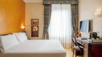 Una habitación de hotel con una cama grande, un escritorio con una silla, un televisor y una lámpara.