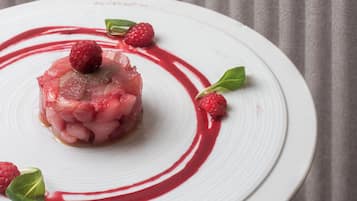 A white plate with a central food item, surrounded by raspberry leaves and a red sauce.