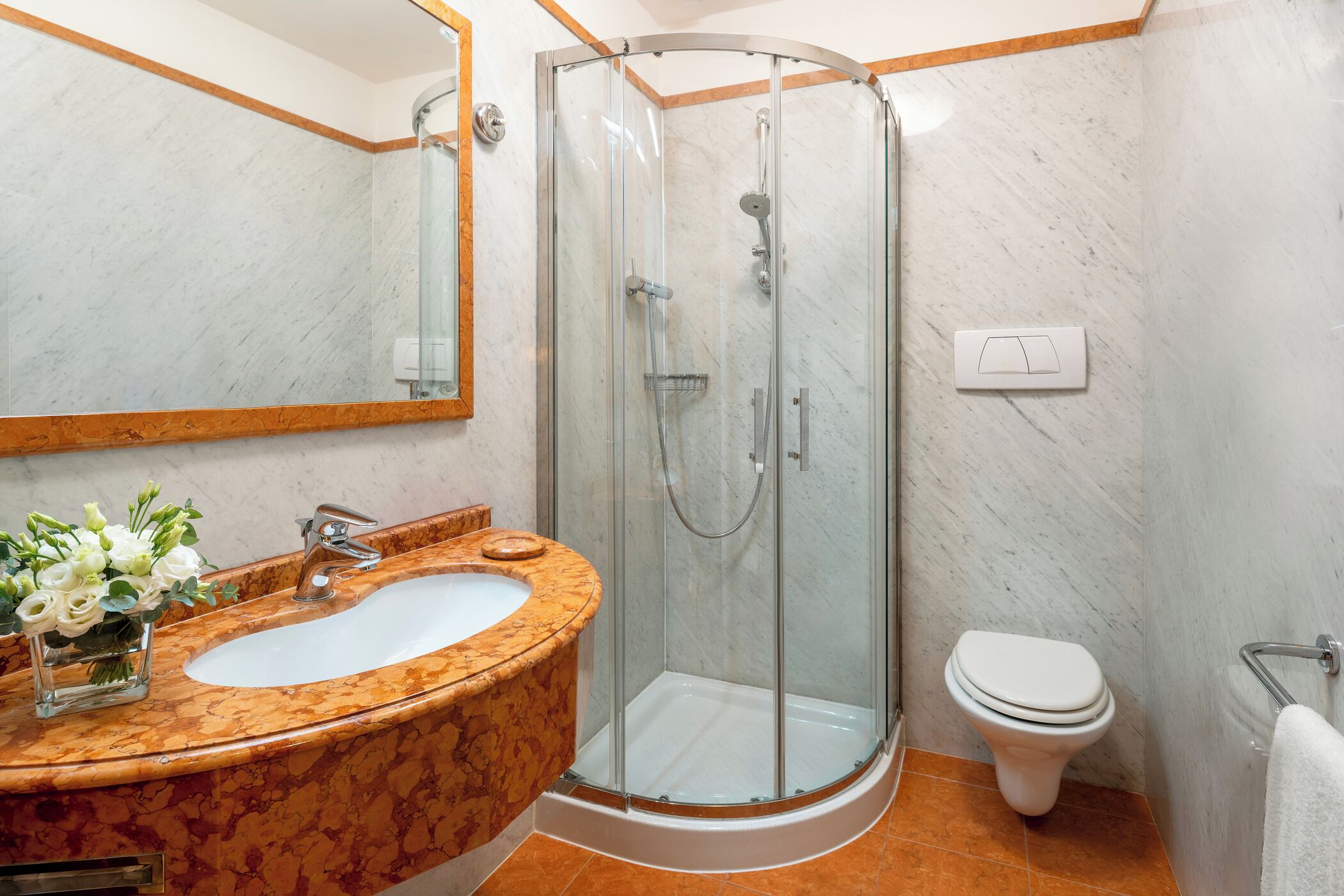 A bathroom with a marble sink, a glass-enclosed shower, and a white toilet.