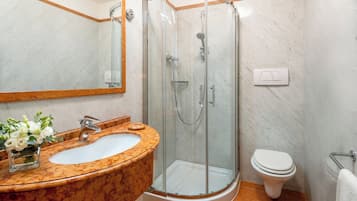 Un baño con lavamanos de mármol, ducha con mampara de vidrio y retrete blanco.