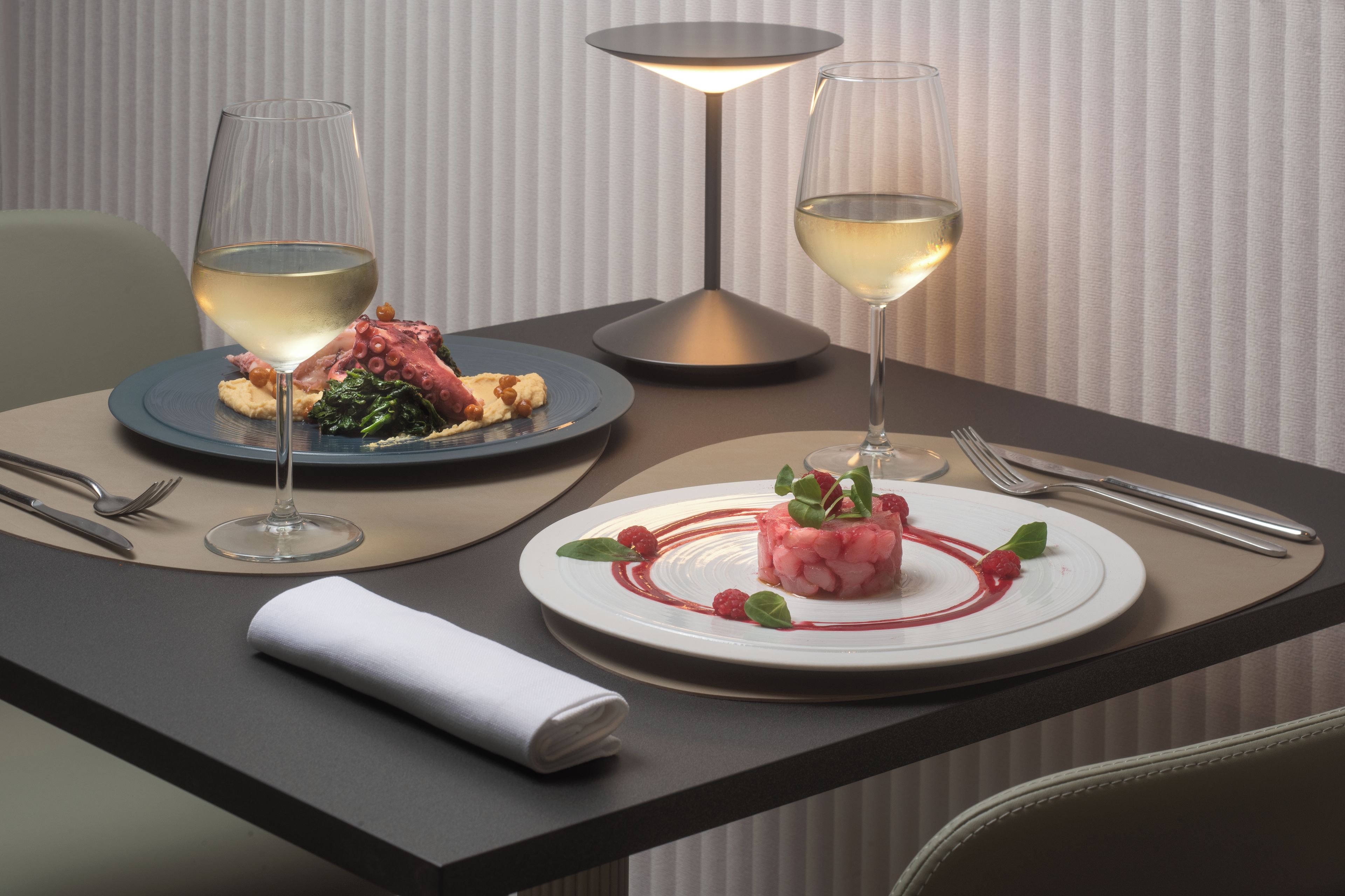 Een eettafel met twee borden eten, twee wijnglazen en een lamp.