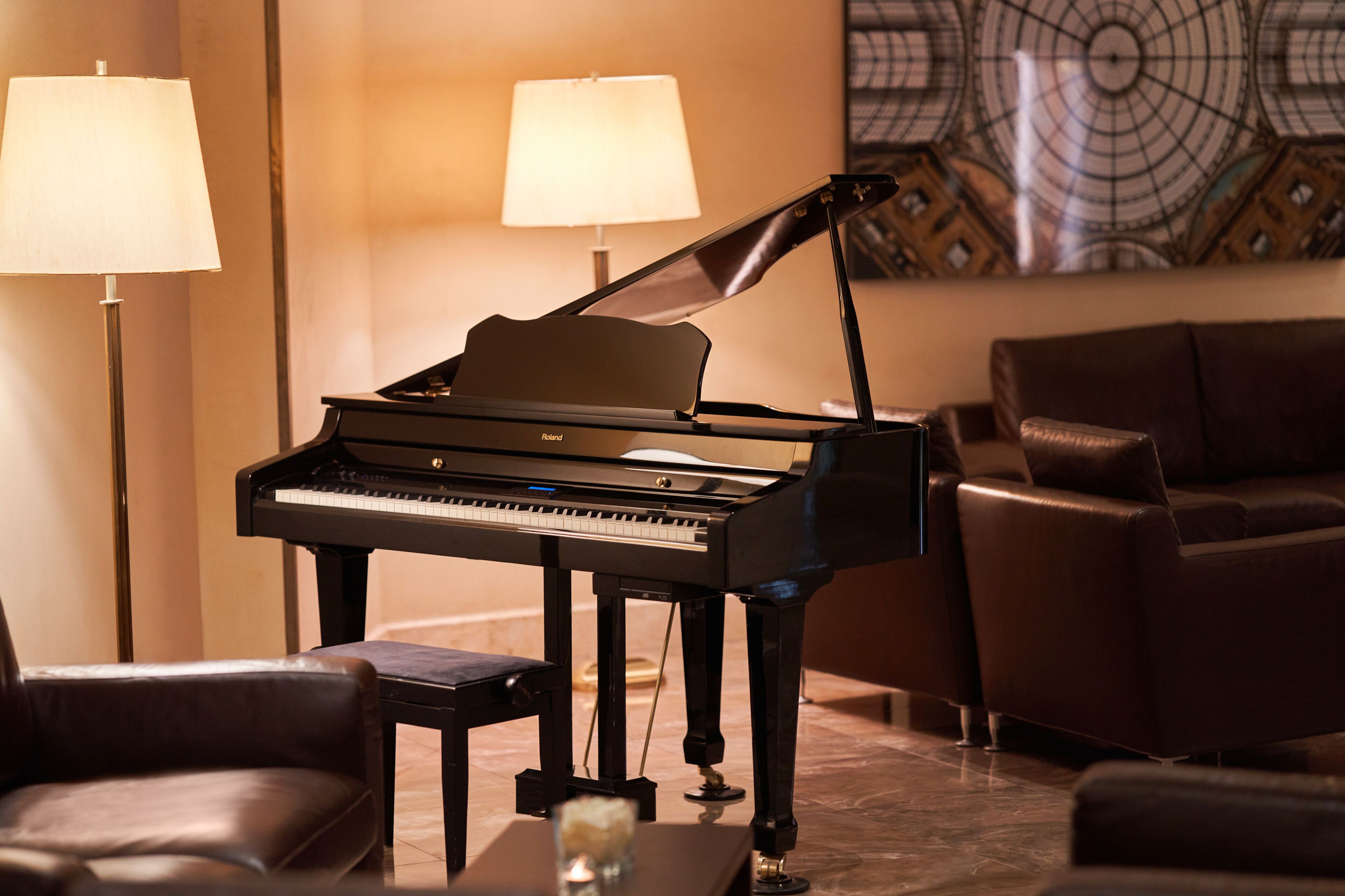 Un piano à queue dans une pièce bien éclairée, avec une lampe moderne et un mur orné d’un motif décoratif.
