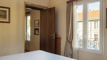 A bedroom with a bed, a wooden door, a window with a view of buildings, and a curtain.