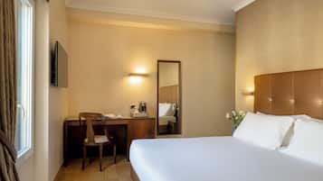 Una camera d'albergo con un letto, una scrivania con una sedia, una macchina del caffè, una TV e uno specchio.