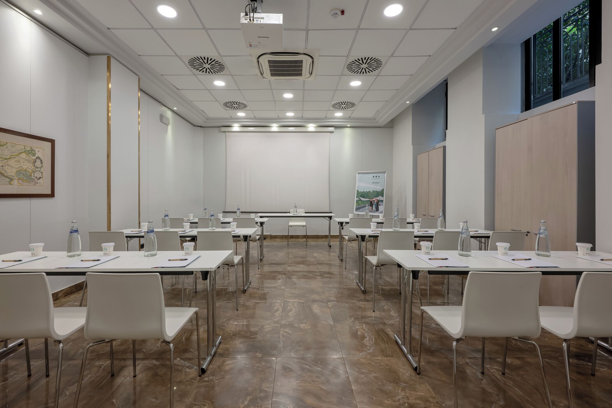 Un salón de conferencias con mesas y sillas blancas, y una pantalla para proyector.