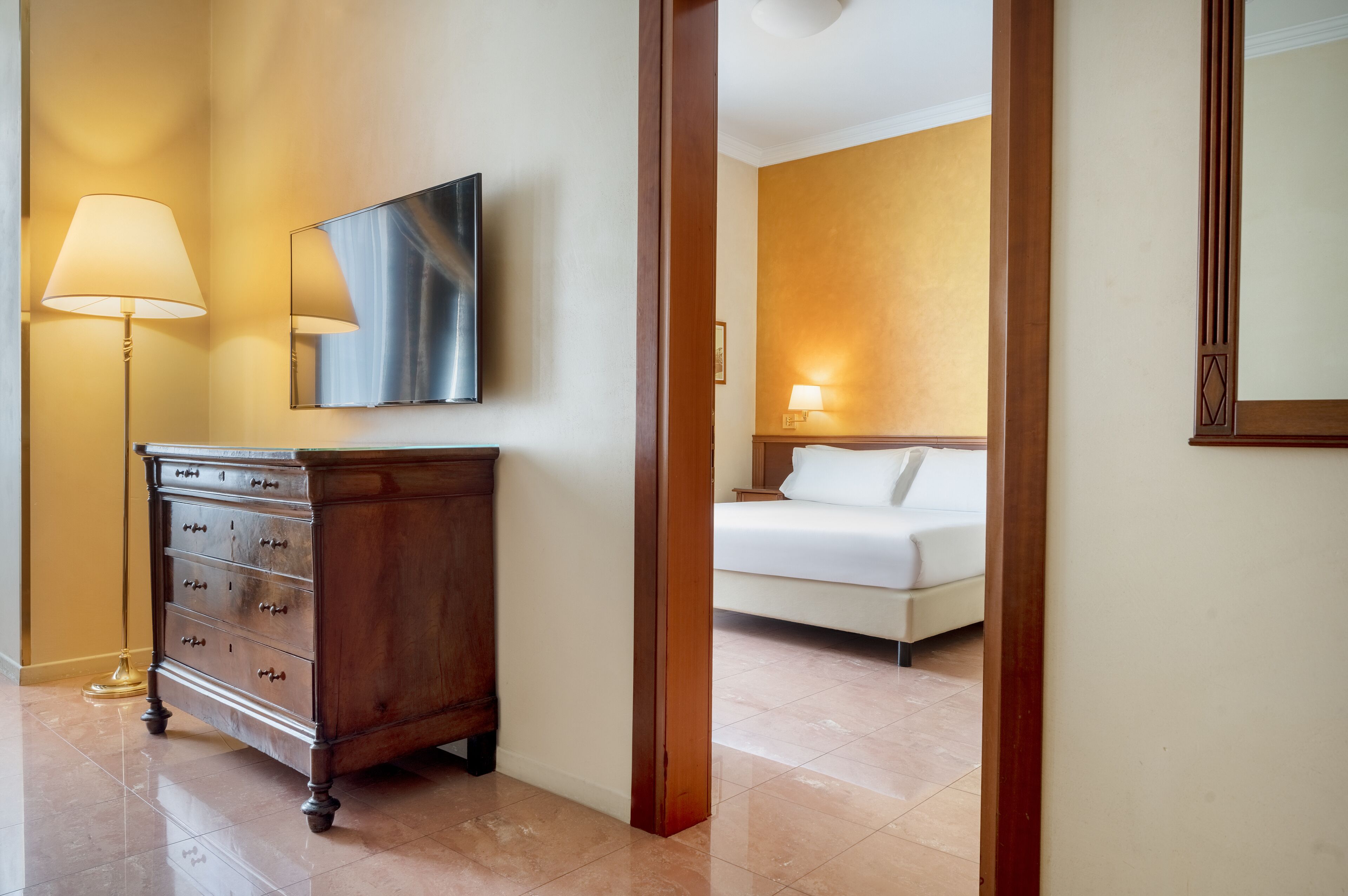 Una habitación de hotel con un aparador de madera, una cama y un televisor montado en la pared.