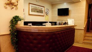 A reception desk with a cushioned back, a clock, and a television on the wall. - Galileo (Rome)