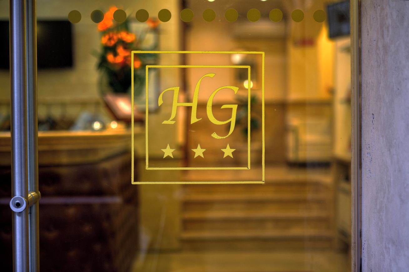 A hotel reception area with a glass door featuring the initials 'HG' and three stars.