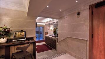 A hotel lobby with a reception desk, a television, a seating area, and a staircase.