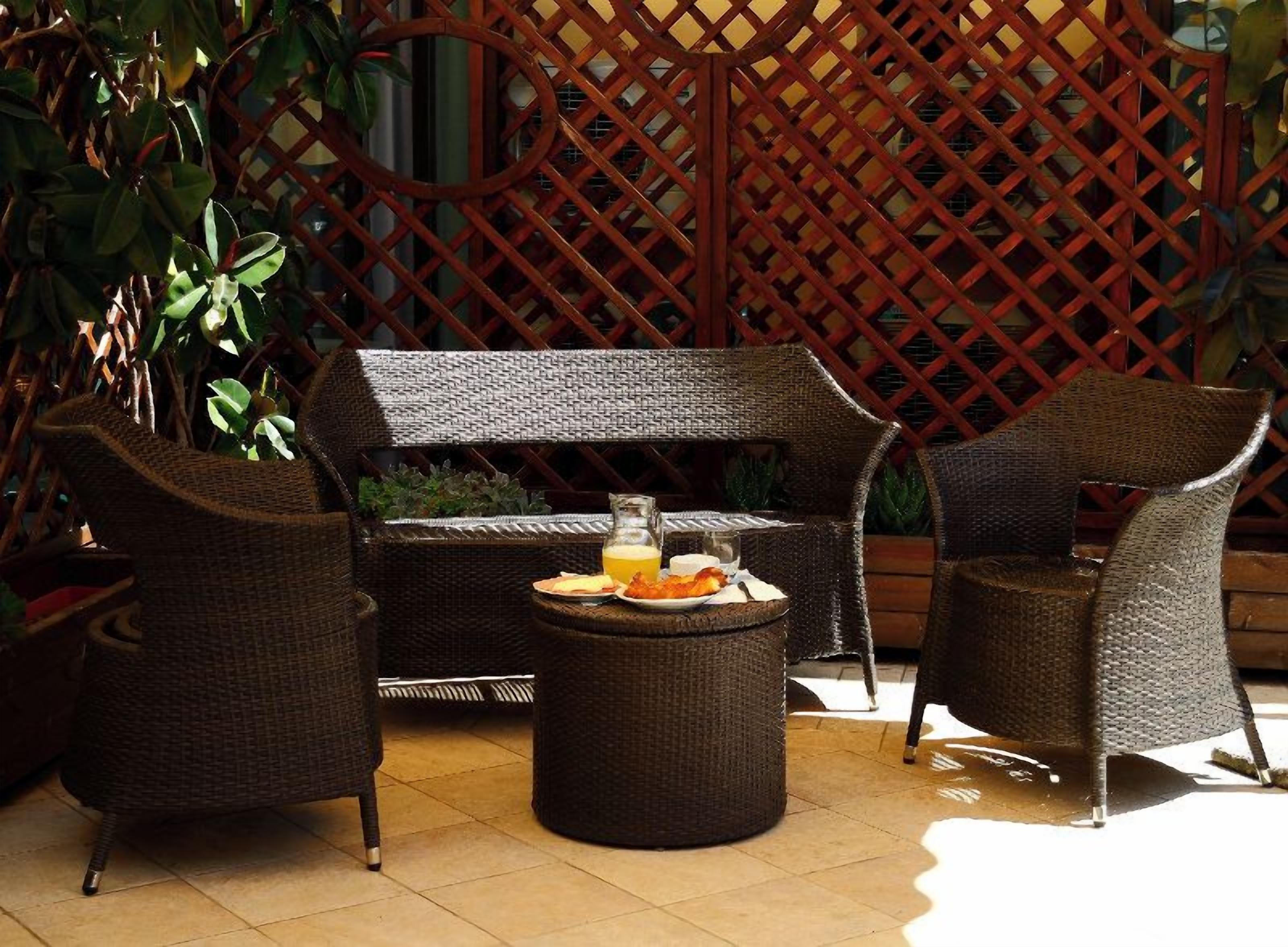An outdoor seating area with wicker furniture, a round table with a drink and snacks, and a lattice backdrop.