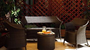 An outdoor seating area with wicker furniture, a round table with a drink and snacks, and a lattice backdrop.