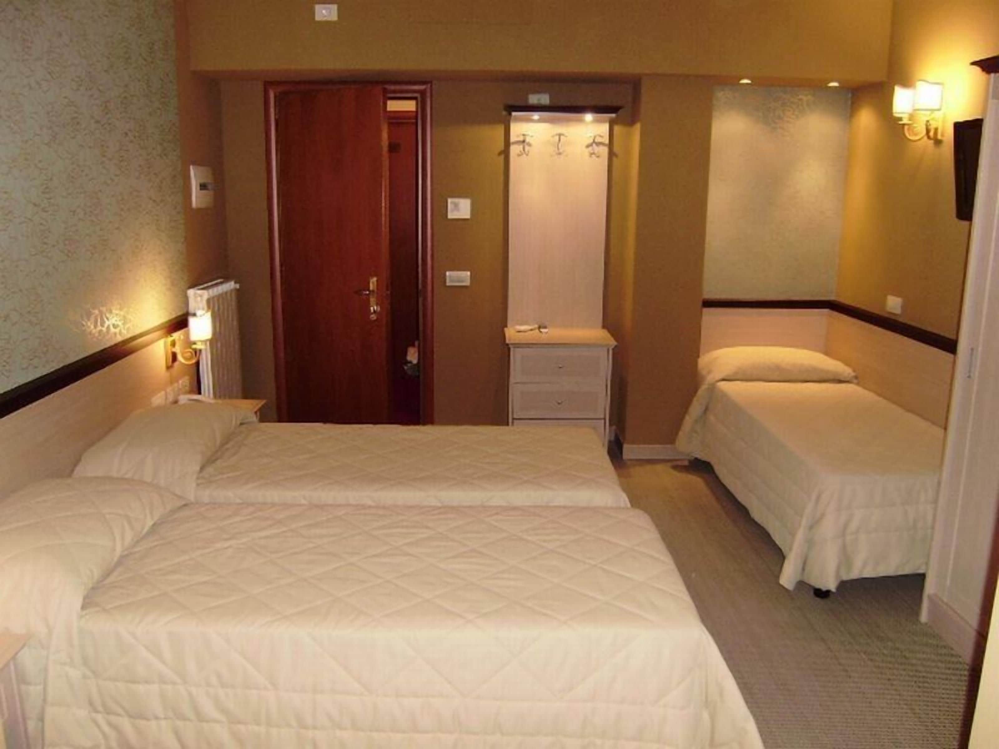 Une chambre d’hôtel avec deux lits, une porte en bois, une petite table de chevet et un luminaire fixé au mur.
