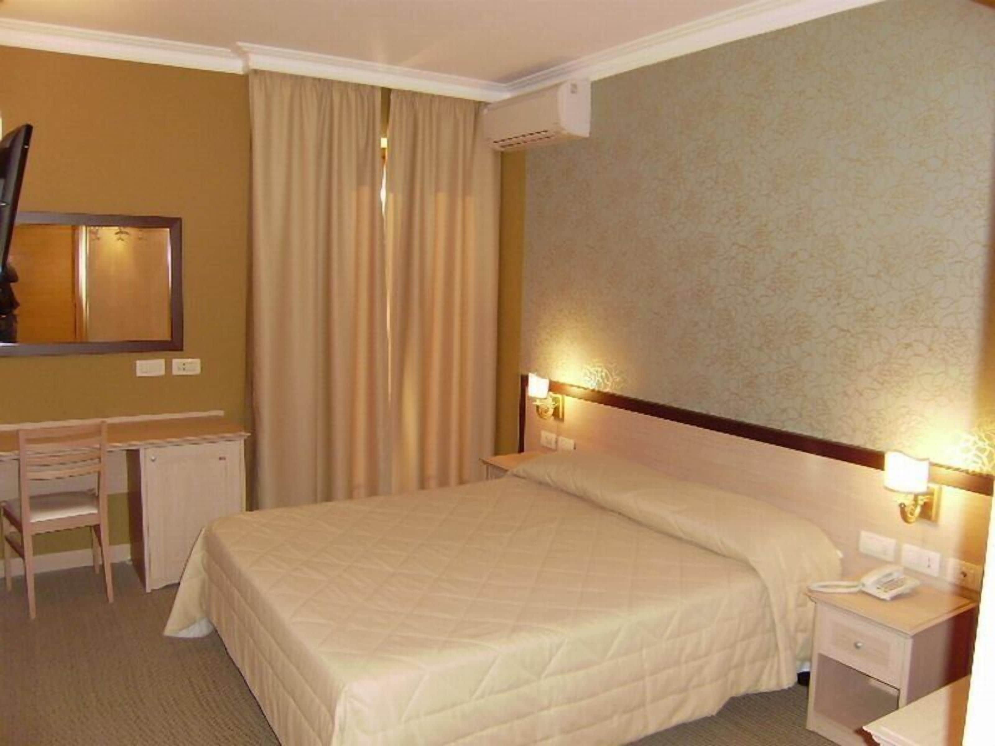 A hotel room with a bed, bedside tables, a desk, and a chair.
