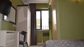 A bedroom with a bed, a desk, a chair, a radiator, and a window with curtains.