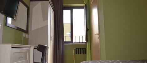 Un dormitorio con cama, escritorio, silla, radiador y ventana con cortinas.