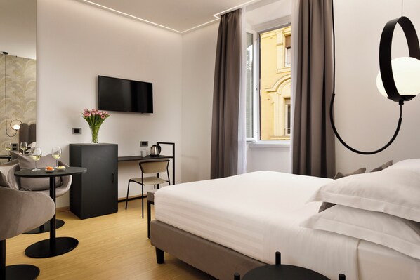 Una habitación de hotel moderna con cama, escritorio, silla, televisor y ventana con cortinas.