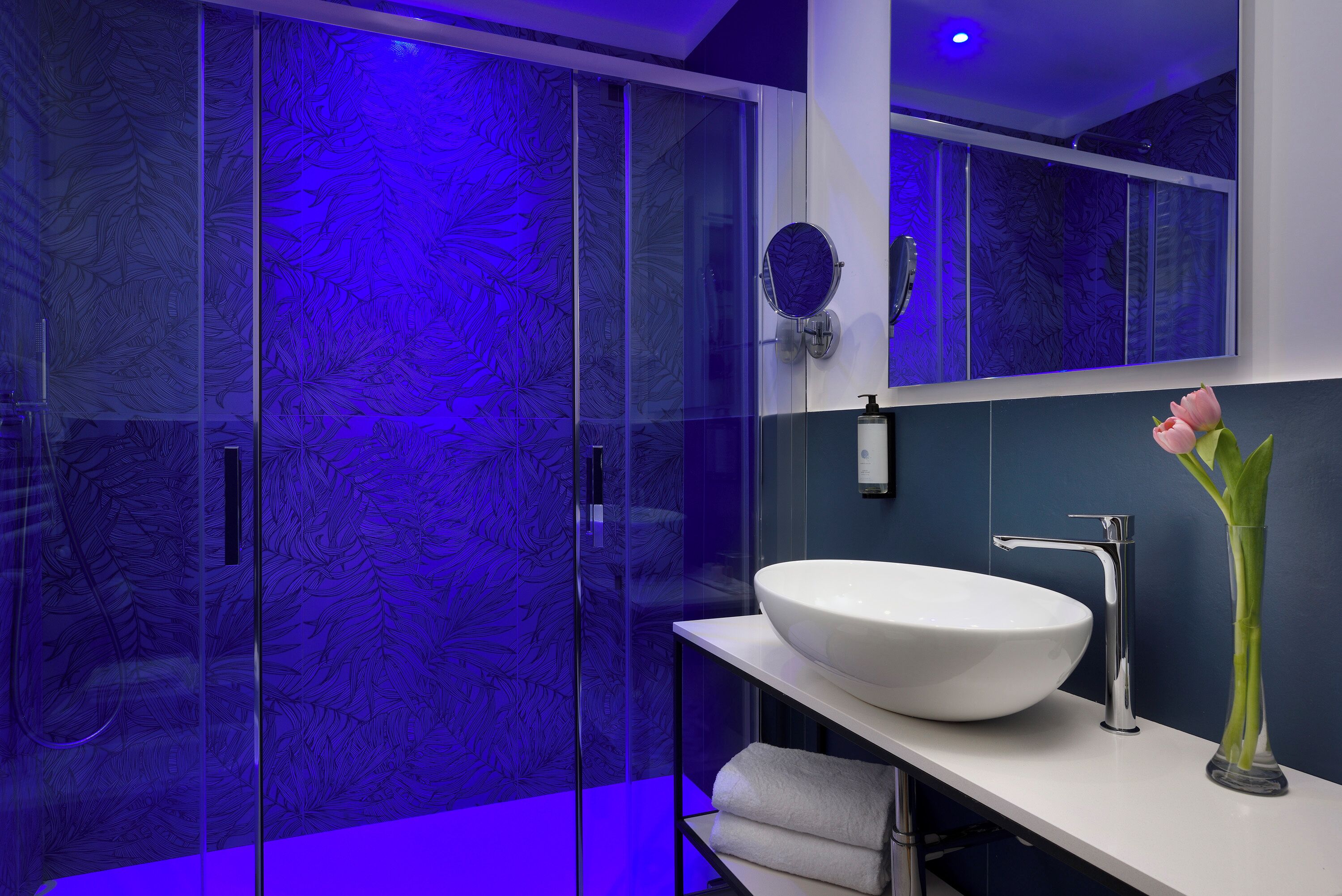 A modern bathroom with a glass shower enclosure, a white sink, and a vase with flowers.