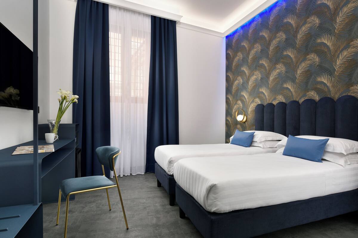 Et hotelværelse med to senge, et skrivebord, en stol og en pyntet væg.