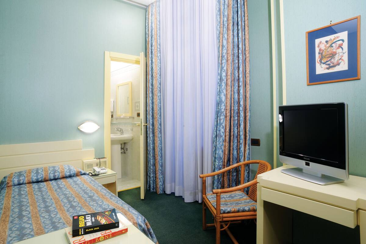 Et hotelværelse med seng, skrivebord med computer, stol, badeværelse med håndvask og brusebad.
