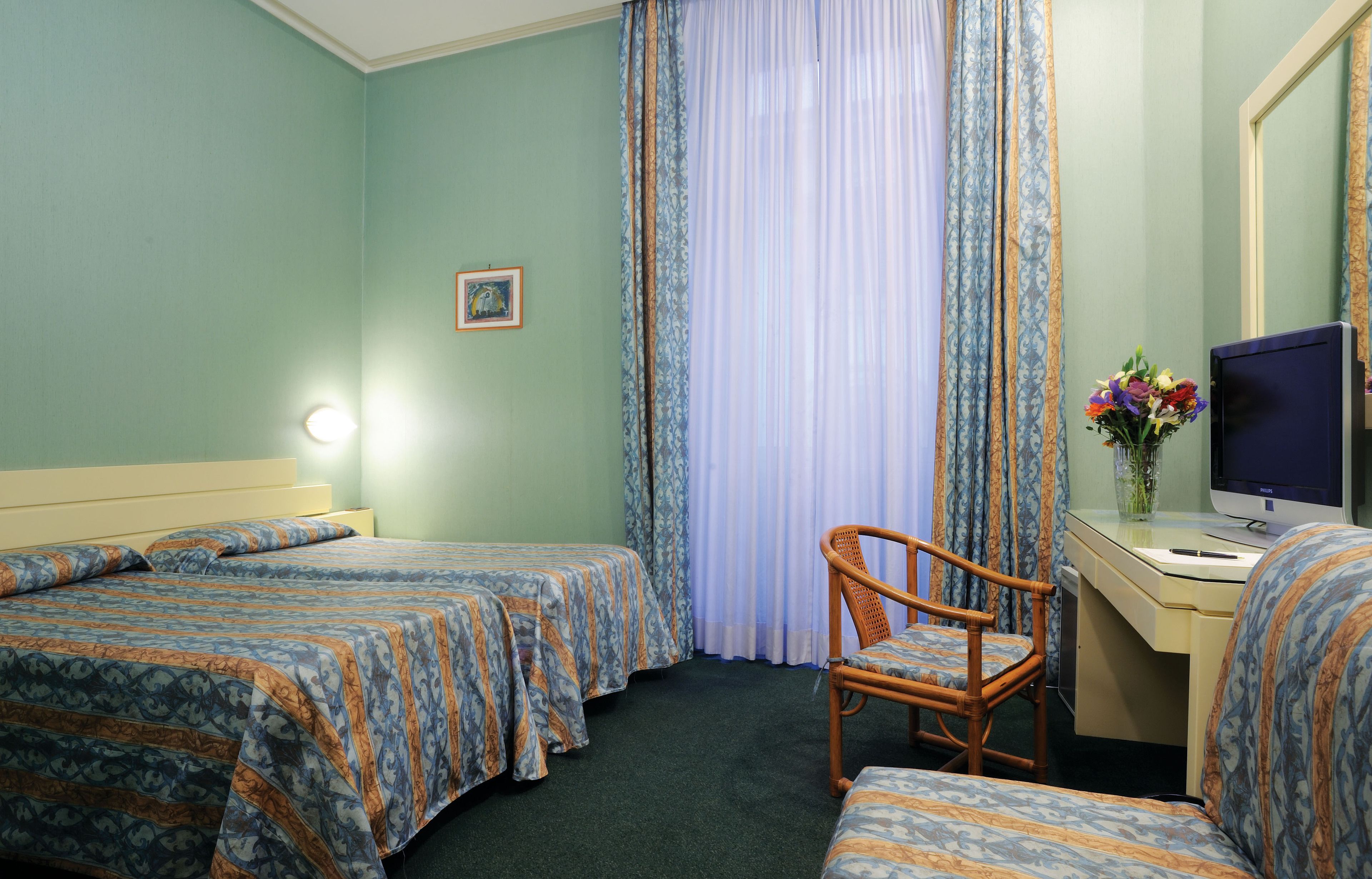 A hotel room with two beds, a desk with a computer, a chair, and a window with curtains.