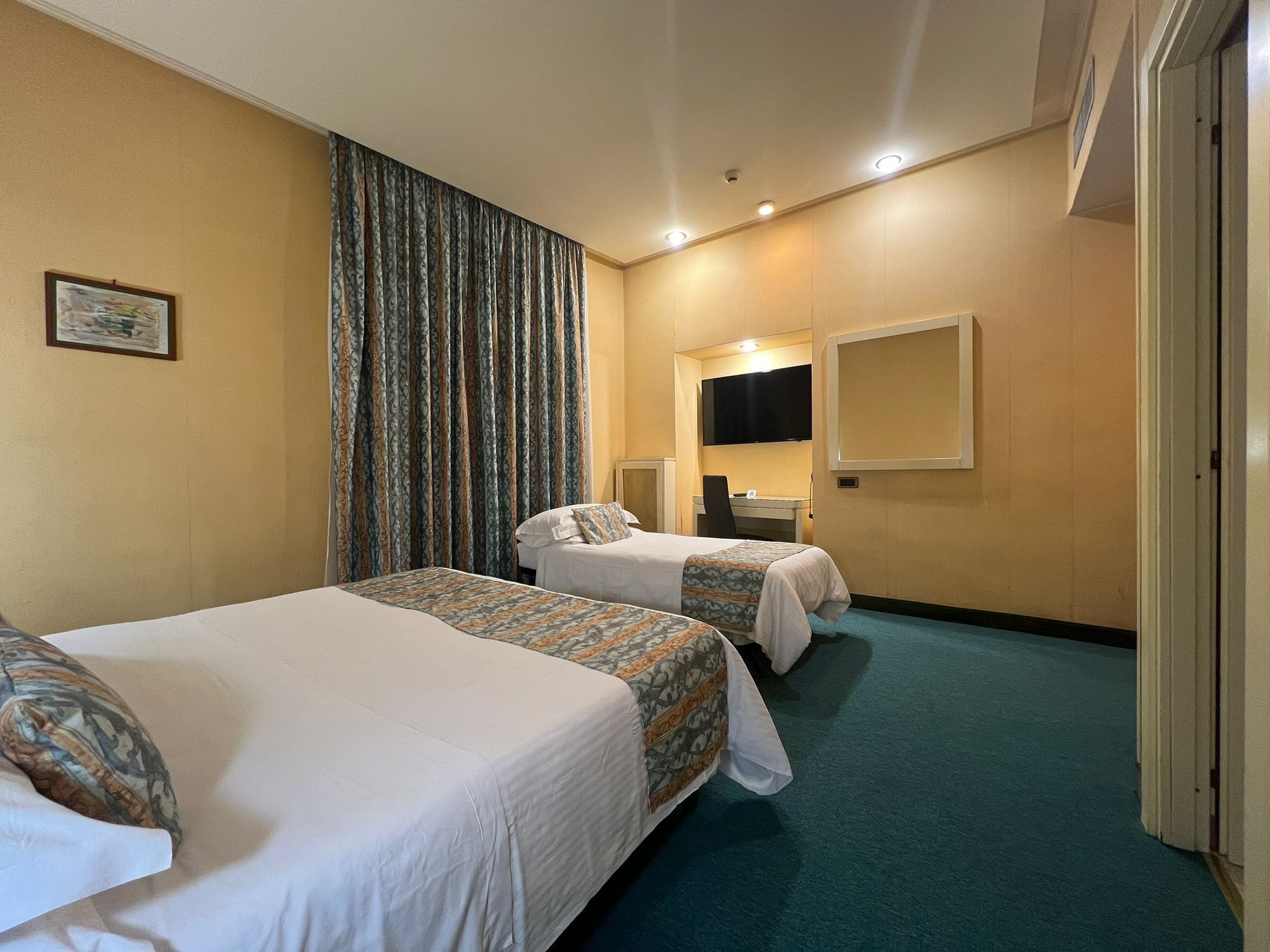A hotel room with two beds, a desk, a chair, a TV, and a large window with curtains.