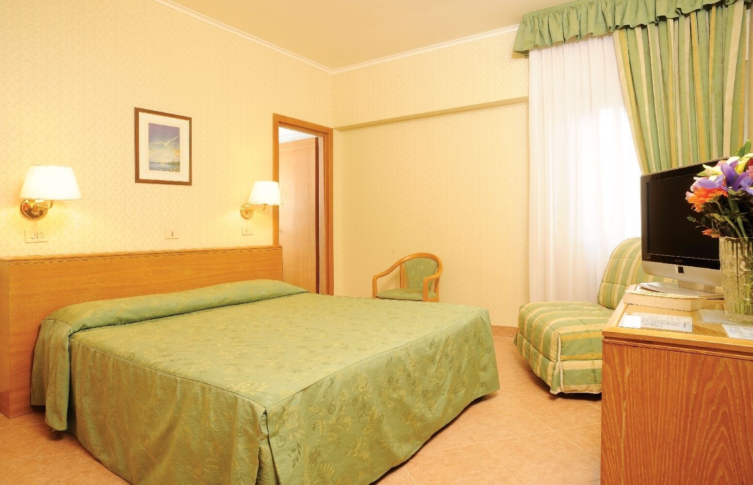 A hotel room with a bed, a chair, a desk with a computer, and a television.