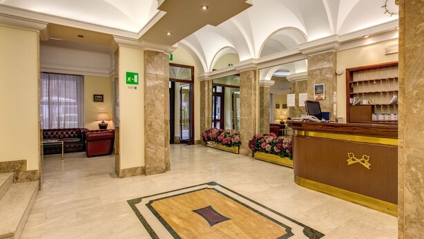 A lobby with marble flooring, a reception desk, a sofa, and a staircase. - Hotel Igea (Rome)