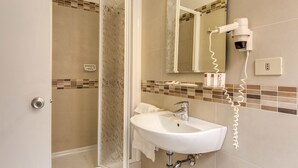 A bathroom with a glass shower door, a sink, a mirror, and a hairdryer on the wall. - Hotel Igea (Rome)