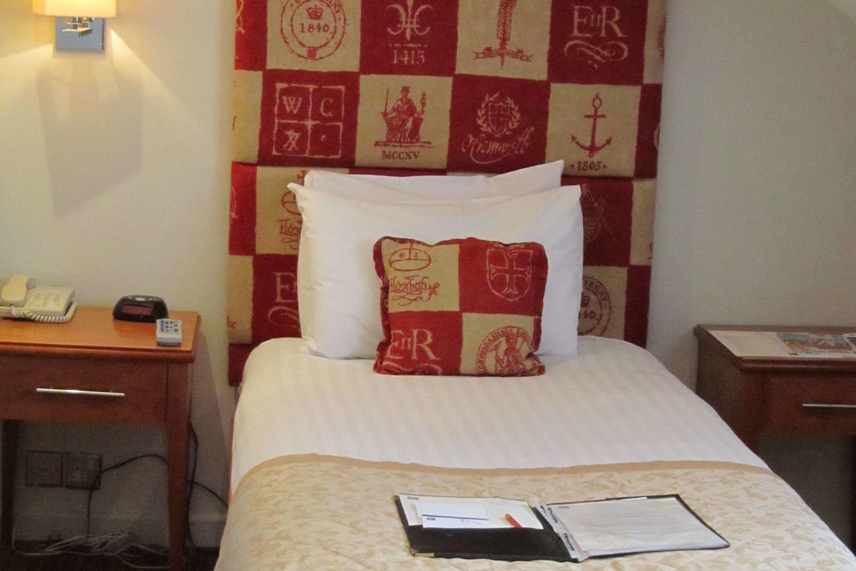 A neatly made bed with a checkered headboard, a bedside table with a lamp, and a phone.