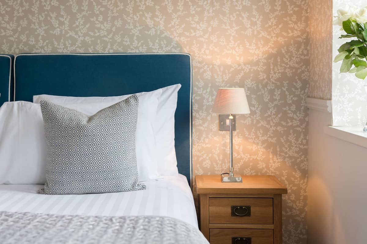 A neatly made bed with patterned pillows, a bedside lamp, and a nightstand with drawers.