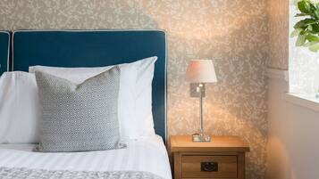 Una cama bien hecha con almohadas estampadas, una lámpara de noche y una mesita de noche con cajones.