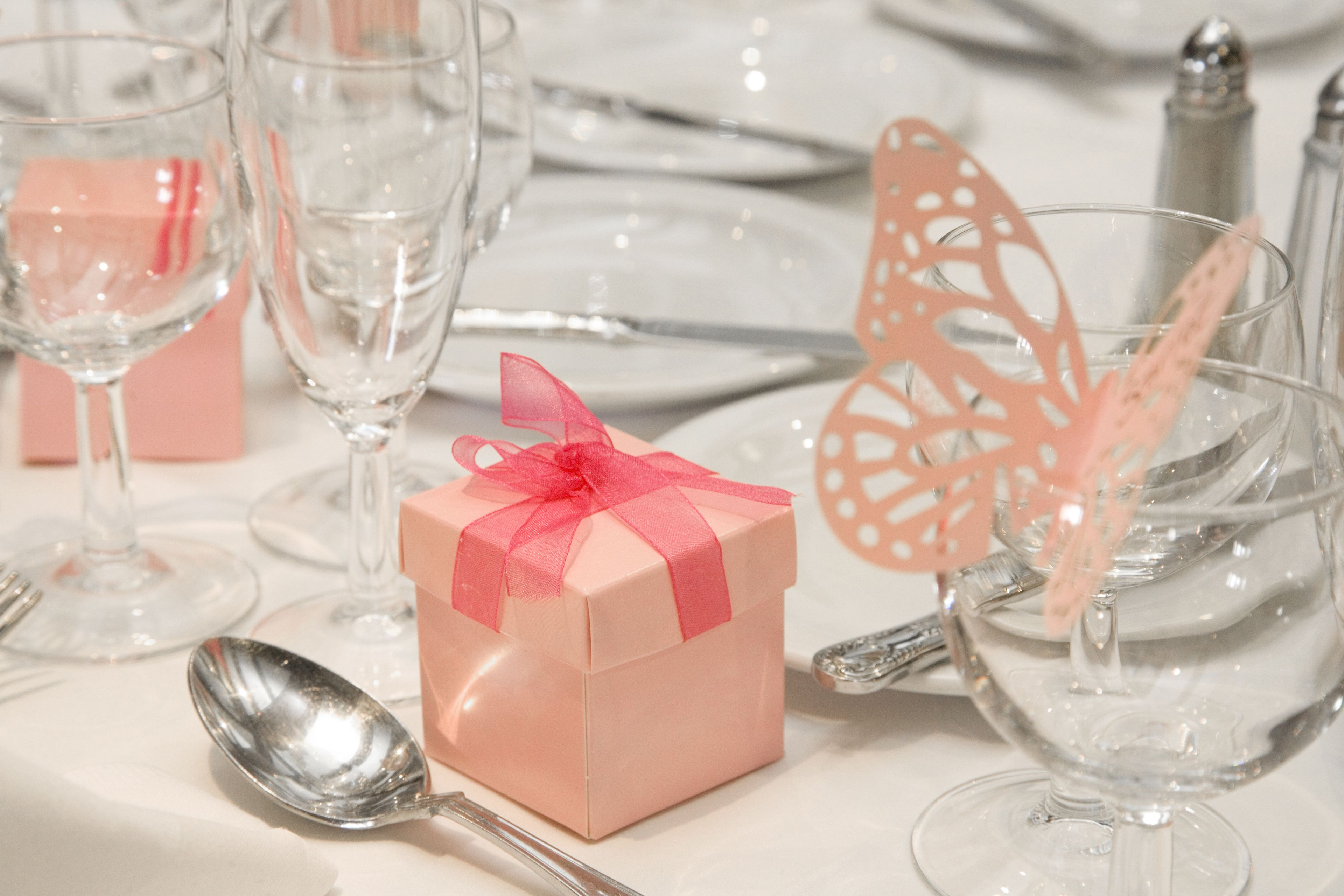 A table set with clear glassware, a pink gift box, and a decorative butterfly ornament.