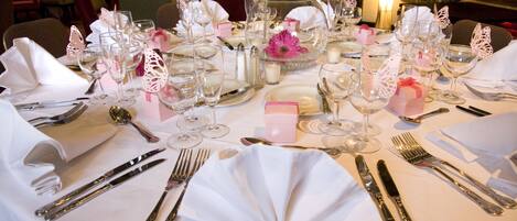 Une table dressée pour un dîner formel, avec plusieurs couverts comprenant assiettes, couverts et verres à vin.