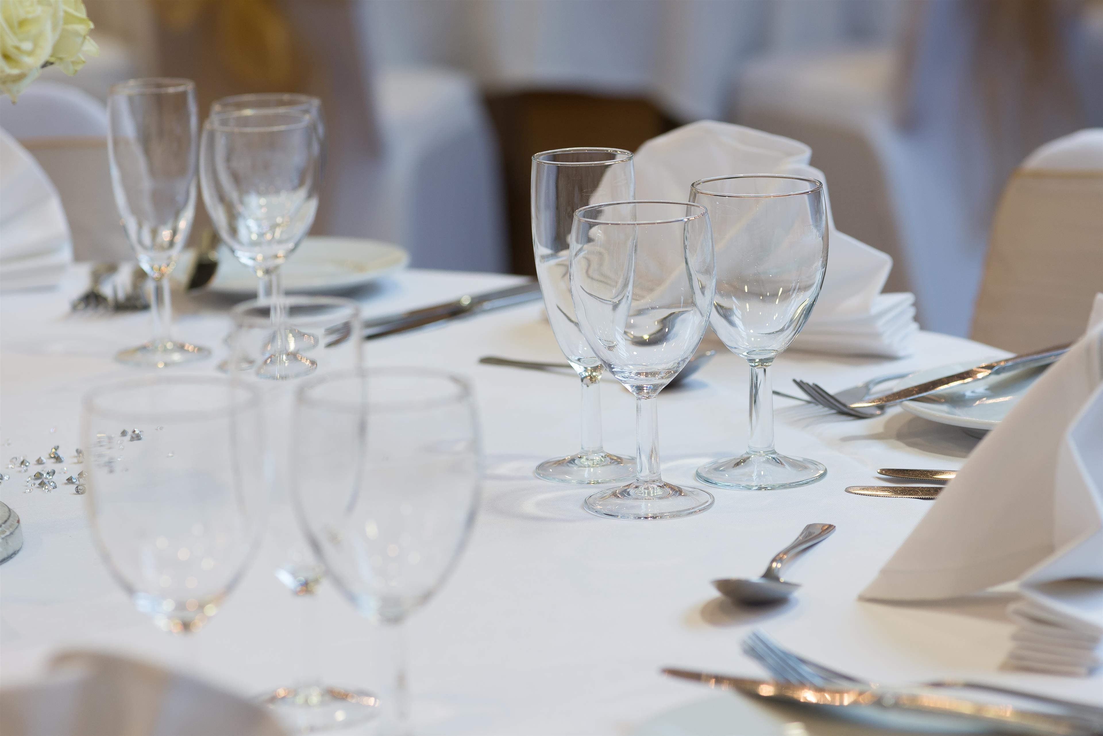 A table set with clear wine glasses, silverware, and white napkins, indicating a formal dining arrangement.