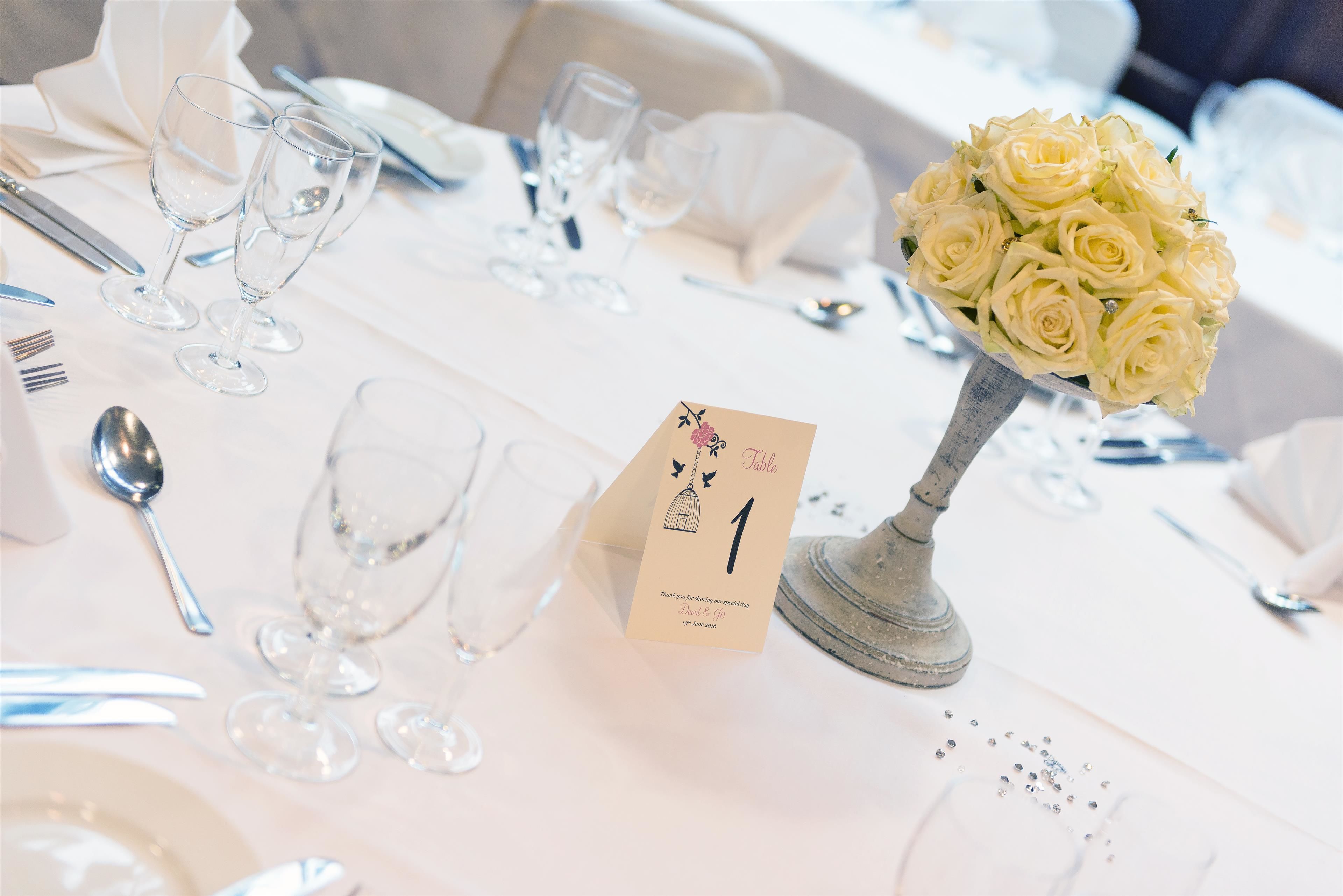 Ein Tisch ist mit einer weißen Tischdecke, klarem Glas und einem Strauß weißer Rosen gedeckt.