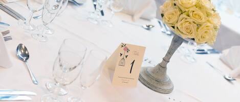 Una mesa dispuesta con mantel blanco, copas transparentes y un ramo de rosas blancas.