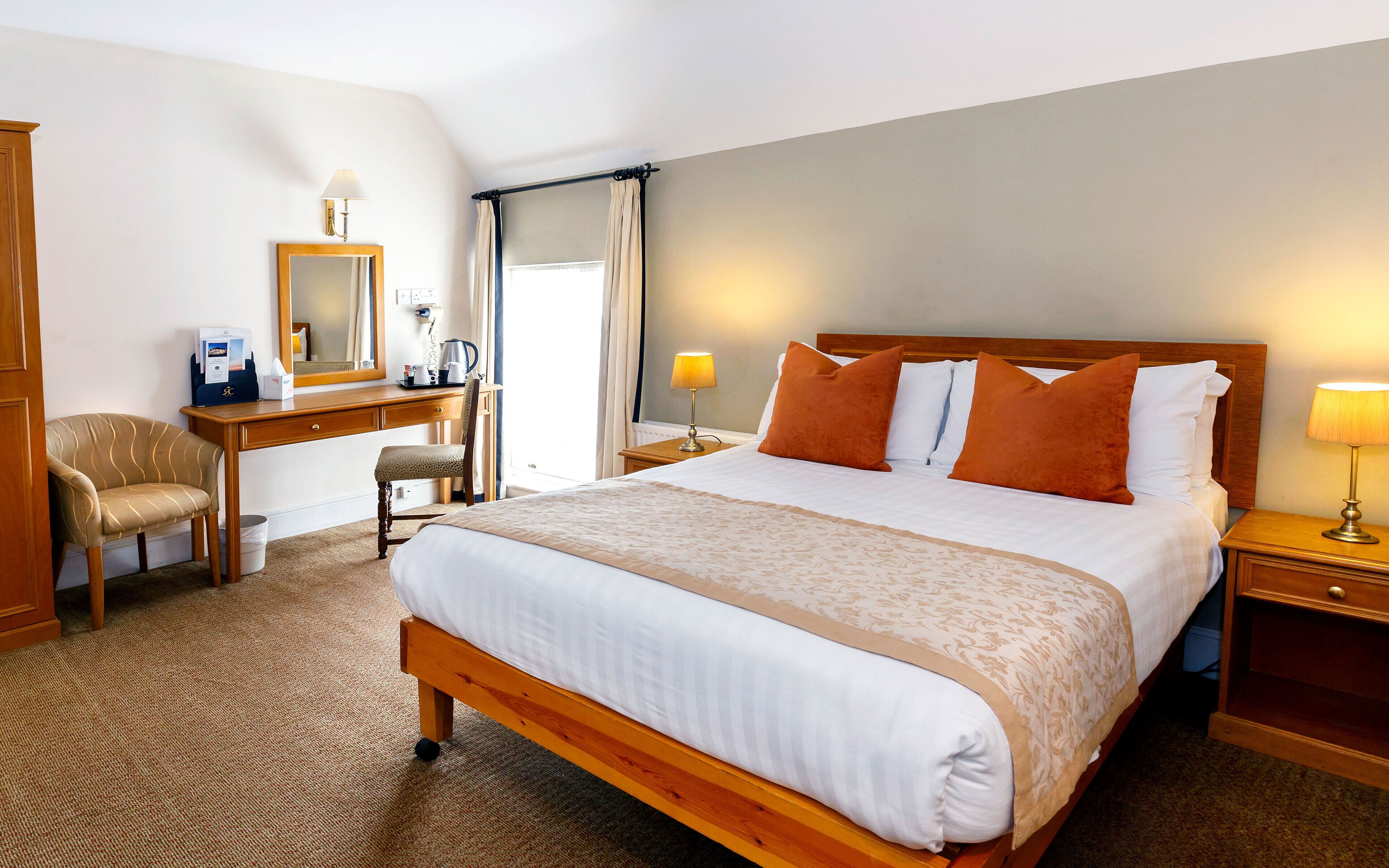 A hotel room with a large bed, a desk with a chair, a mirror, and two bedside lamps.