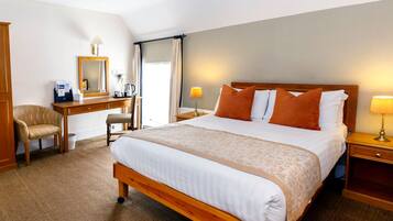 A hotel room with a large bed, a desk with a chair, a mirror, and two bedside lamps.