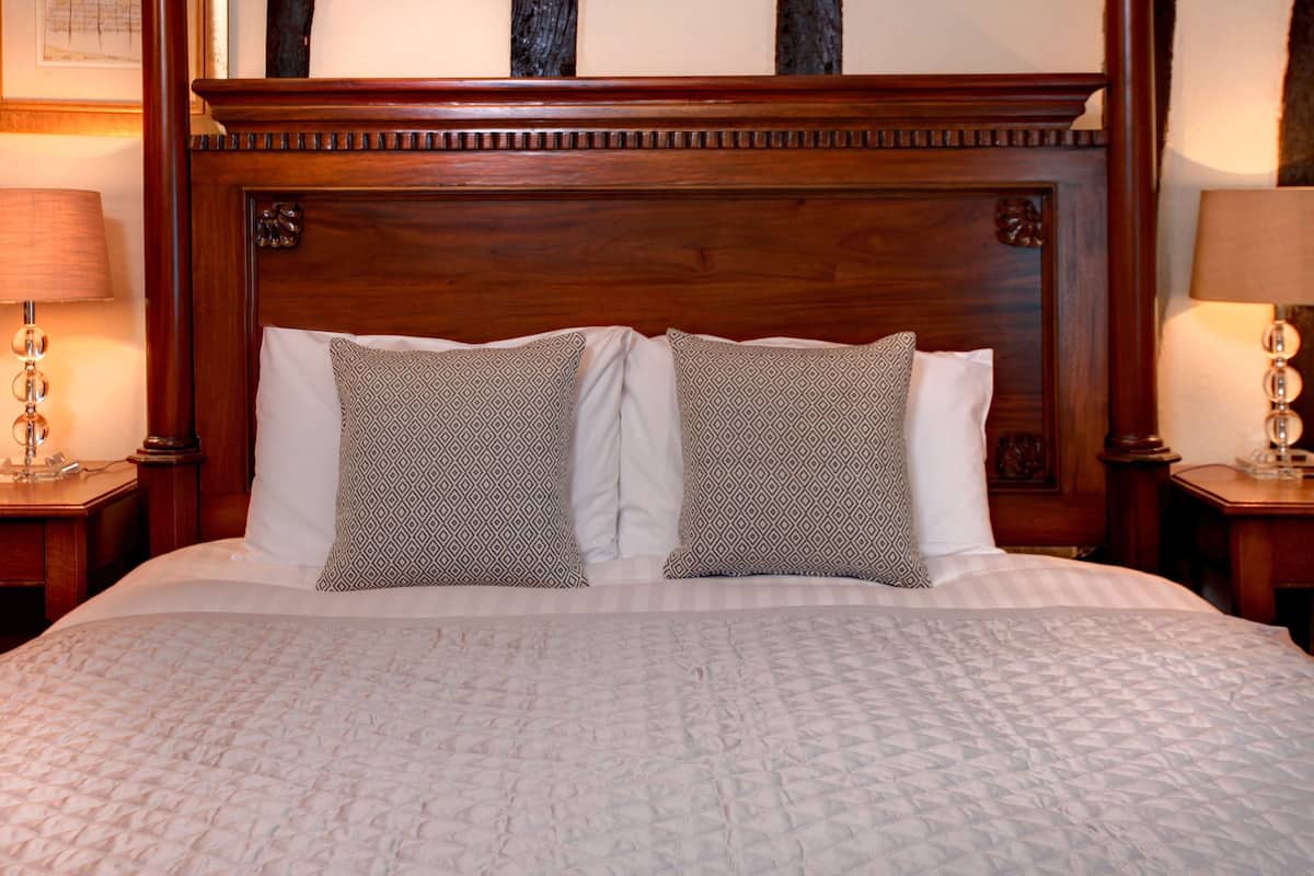 A large bed with a wooden headboard, two patterned pillows, and a quilted bedspread.