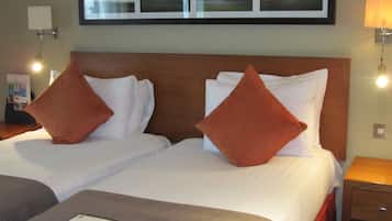 A hotel room with two beds, each with white linens and a wooden headboard. There are two wall-mounted lamps on either side of the beds.
