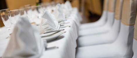 A long table with white tablecloths, neatly set with plates, glasses, and cutlery.