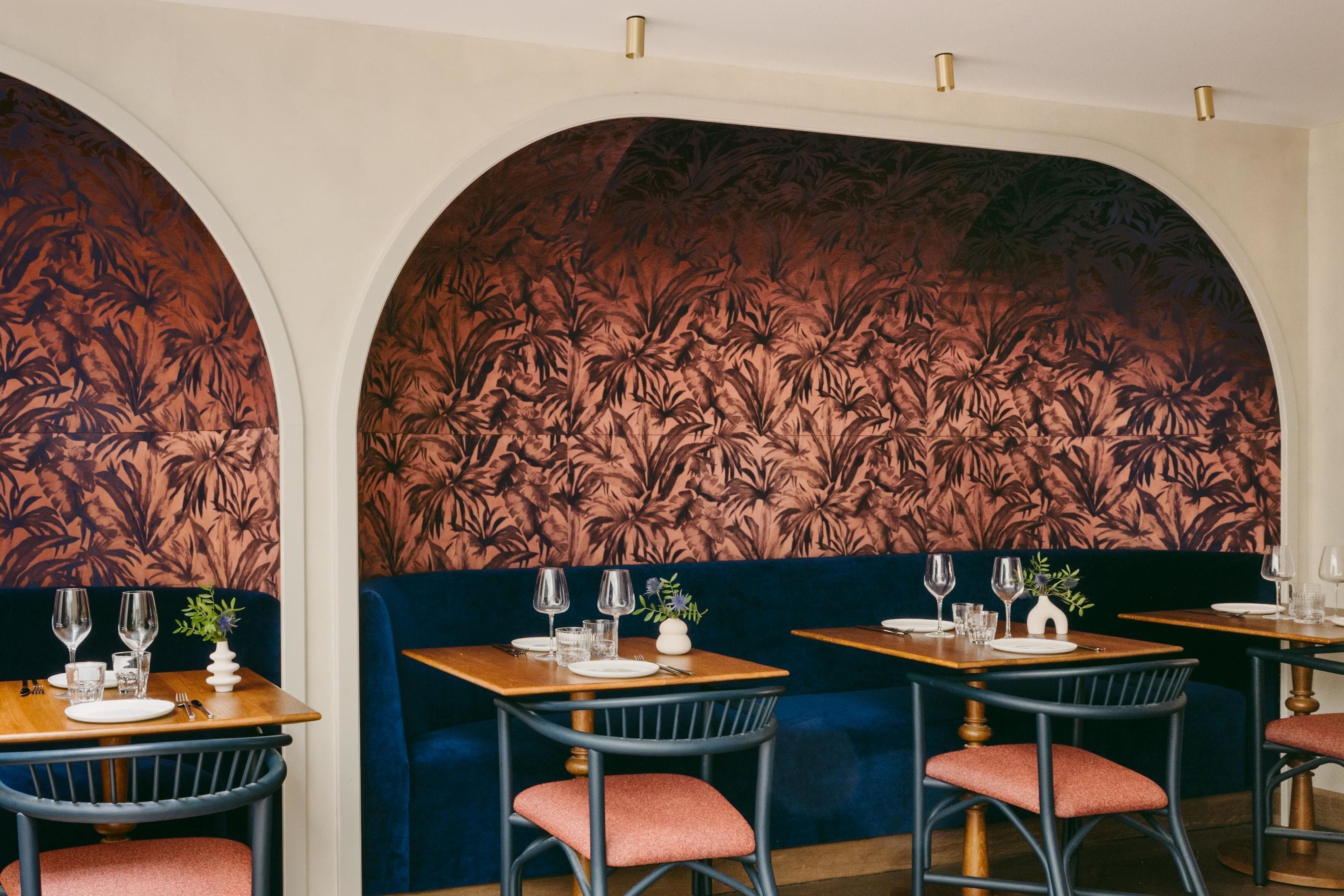 Ein Restaurantinnenraum mit dunkelblauen Sitzbänken, Holztischen und einem floralen Wanddesign.