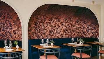 Ein Restaurantinnenraum mit dunkelblauen Sitzbänken, Holztischen und einem floralen Wanddesign.