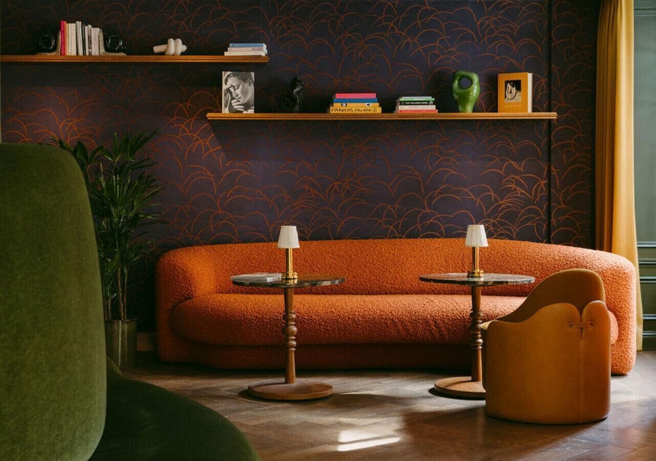 A cozy living room with a vibrant orange sofa, two side tables, and a green armchair.